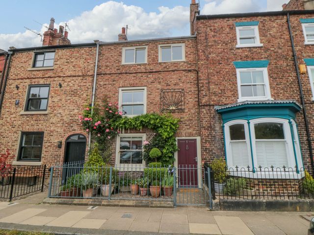 A brick residential house with potted plants and a red door at 5 College Square in Stokesley