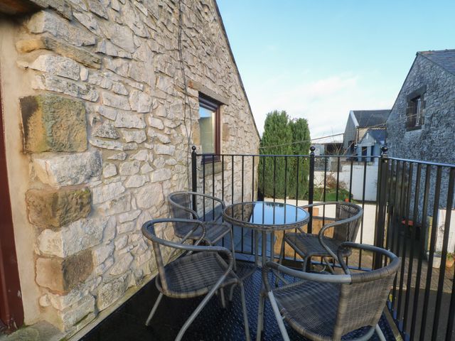 A small outdoor patio with a round glass table and four woven chairs next to a stone wall at The Loft in Buxton