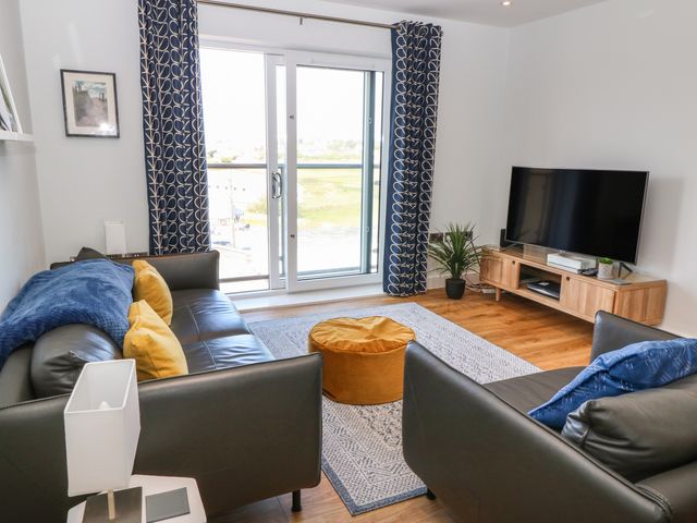 A living room with two black leather sofas a yellow pouf and a television on a wooden stand at Beach Apartment 9 in Trearddur Bay