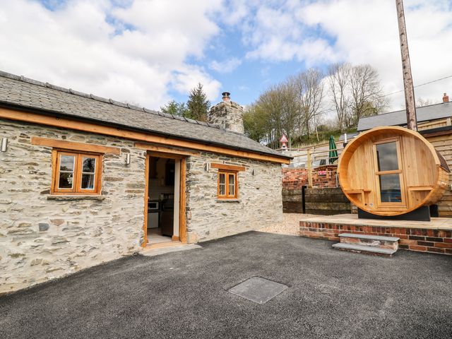 Exterior of a stone cottage with wooden windows and door next to a wooden barrel sauna at The Old Cobblers Shop in Llanbister near Llandrindod Wells