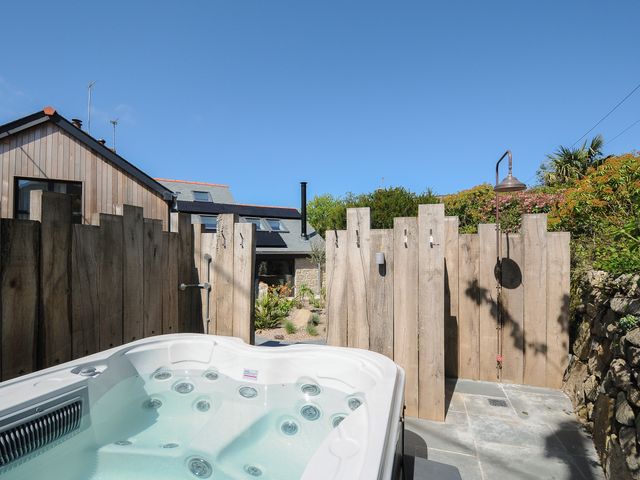 An outdoor hot tub and wooden fence with an outdoor shower in a garden area at Stargazy Cottage in Praa Sands