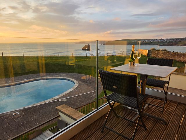 A balcony with a table and two chairs overlooking a pool and the ocean at 7 Ocean's Edge in Thurlestone
