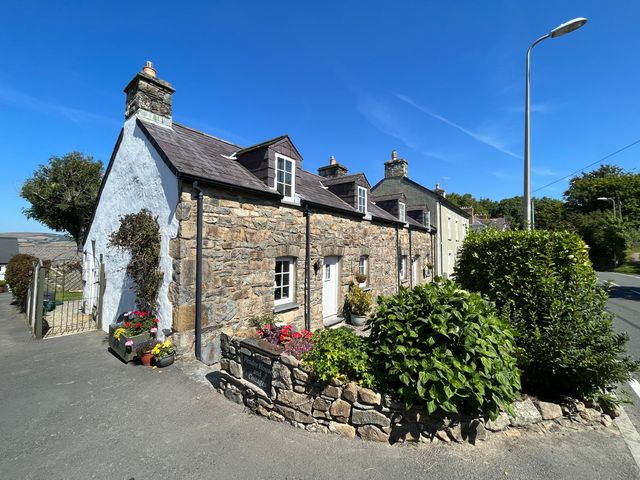 A stone cottage with dormer windows and a garden with bushes and flowers on a street corner at End Cottage Newport Pembrokeshire
