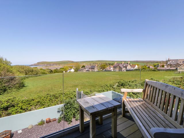 An outdoor area with a bench and table overlooking a field and houses at The Willows in Newport, Pembrokeshire