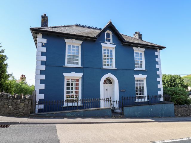 A blue two story house with white window frames and a white door behind a black iron fence Dewi Villa Aberarth Ceredigion
