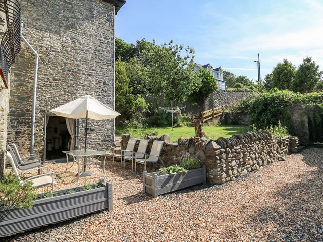An outdoor patio area with chairs a table an umbrella stone walls gravel ground and a grassy garden at Dewi Villa in Aberarth Ceredigion