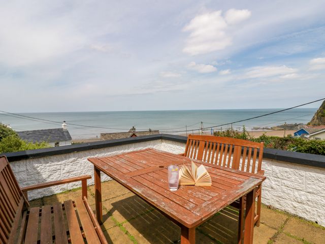 An outdoor seating area with a table, chairs, book, and glass overlooking the sea at Delyn Aur, Tresaith, Ceredigion