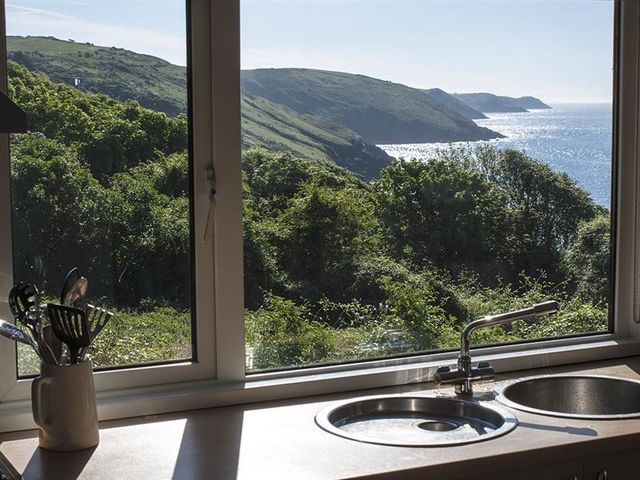 A kitchen sink and utensils on a counter with a window view of green hills and the sea at Beach Cove in Freshwater East Pembrokeshire