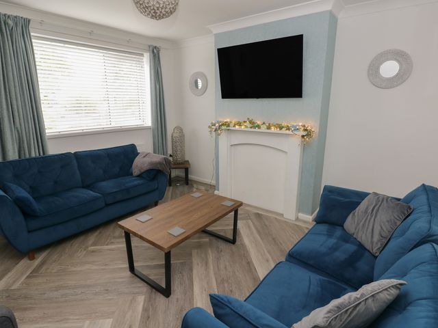 A living room with blue sofas and a coffee table at Cwtch Ar Y Mor in Burry Port