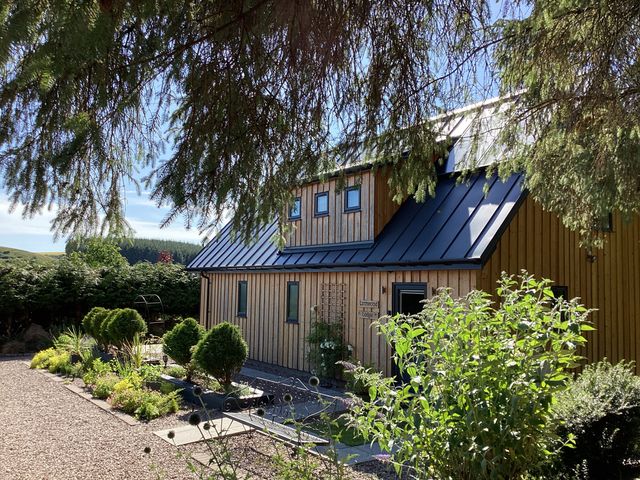 A wooden building with a black roof and garden at Larchwood Lodge in Ellon