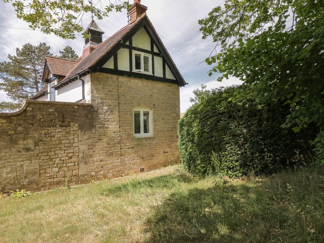 Stone house with white windows and a tiled roof near a stone wall and green hedge at The Coach House in Box near Minchinhampton