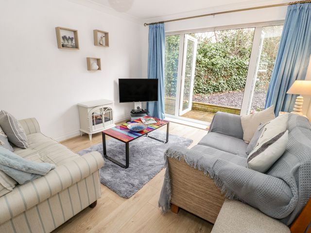 A living room with two sofas a colorful coffee table a TV and large windows with blue curtains at 10 The Orchard in Rhos-On-Sea