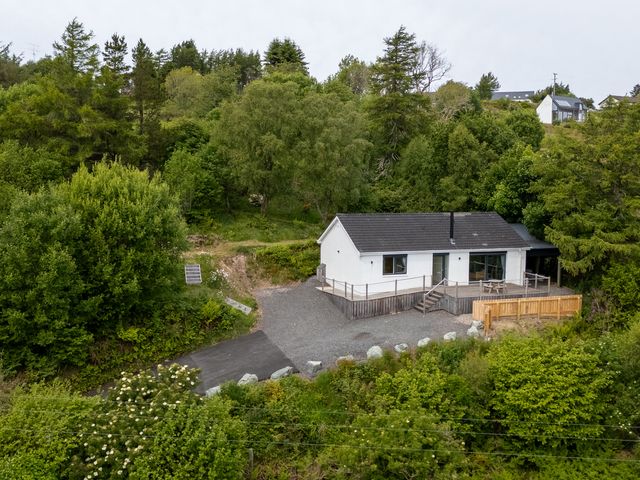 A white house with a gray roof surrounded by trees and greenery at The Lookout in Saasaig near Broadford