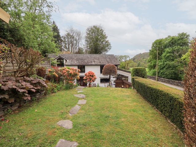 A garden with a stone pathway leading to a white house with trees and hedges around at Old Coach House Ambleside