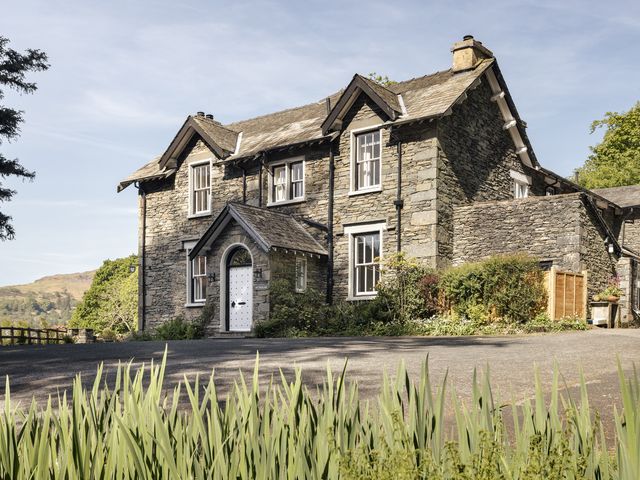 A stone house with white framed windows and a white door surrounded by plants and trees at Wetherlam in Grasmere