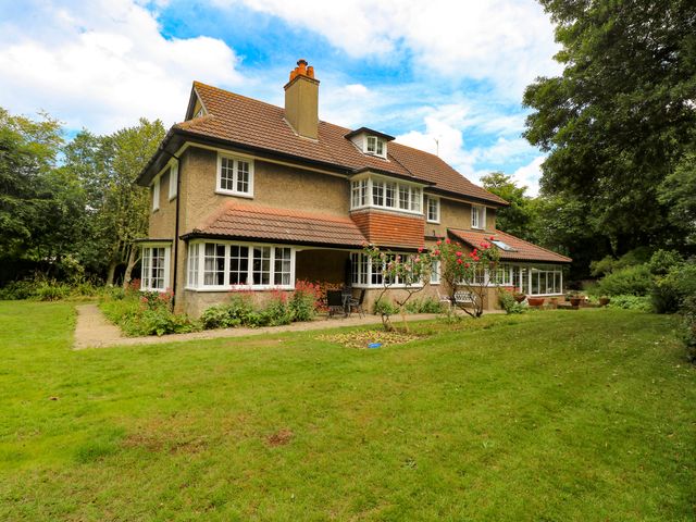A two story house with a tiled roof surrounded by grass and trees at Beckhythe Cottage in Overstrand