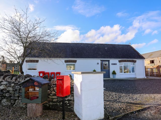 A single-story white house with a dark roof a blue door red post box and small wooden egg box outside Nant y Gof in Cemaes Bay