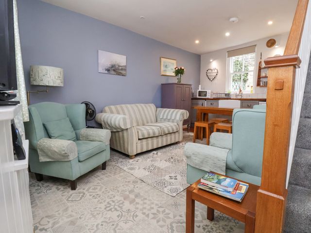 A combined living room and kitchen with armchairs a sofa a wooden dining table and stairs at Millgate Cottage in Conwy