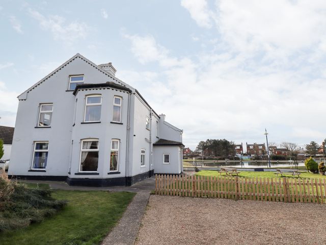 A white two-story house with windows by a fenced grassy area and a gravel path at Bank House in Mablethorpe