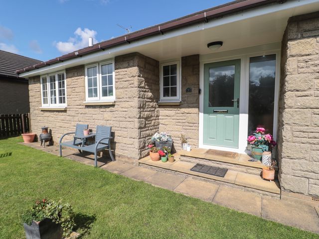The front entrance of a stone house with a green door a bench and potted plants on a patio at Island View Cottage in High Hauxley near Amble