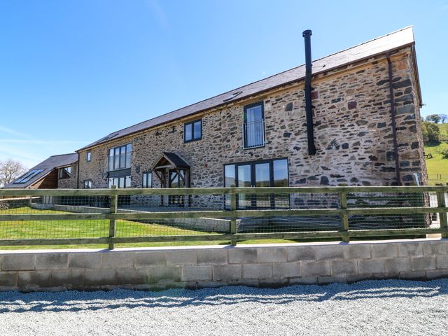 A stone building with multiple windows a wooden fence and grass at Bwthyn Y Bugail Shepherds Cottage in Pedairffordd near Llanrhaeadr-Ym-Mochnant
