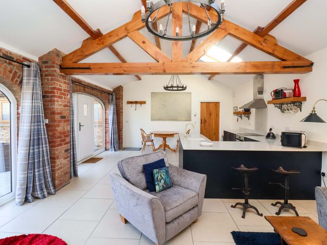 An open plan living room and kitchen with exposed wooden beams brick walls and a gray armchair at Kingfisher Corner in Little Kelk near Bridlington
