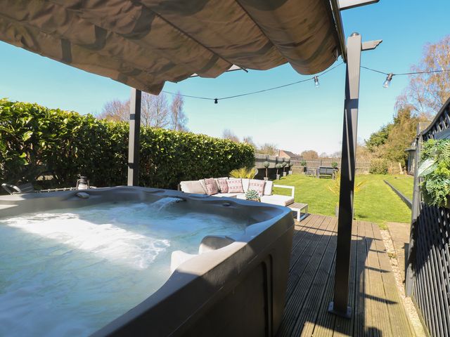 An outdoor patio with a hot tub a sofa with cushions and a garden area at Coupling Cottage in Belper