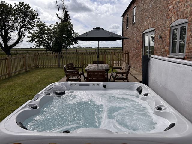 A hot tub and a wooden dining table with chairs in the garden at Acacia Barn in Wrangle near Friskney