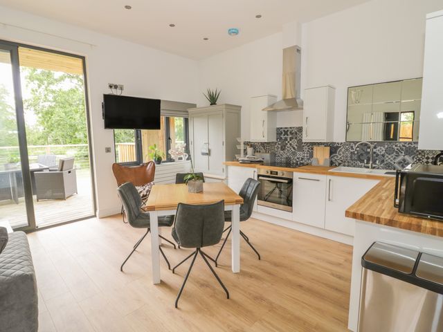 A kitchen and dining area with a wooden table and chairs a wall-mounted tv and sliding glass doors leading outside at The Leat in Droitwich Spa