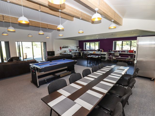 A large room with a long dining table with chairs a pool table couches and an open kitchen at Dales Lodge in Ingleton