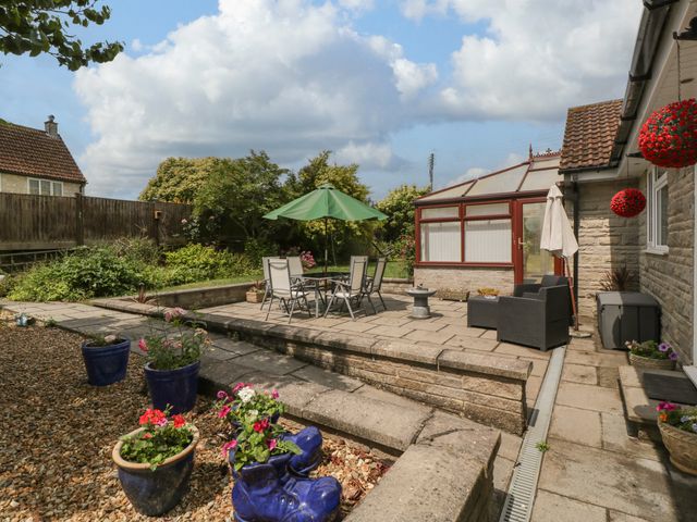 An outdoor patio with a table and chairs under a green umbrella and potted plants on gravel at Melita in Curry Rivel