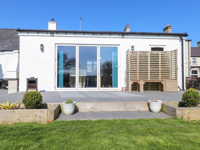 A patio area with a glass sliding door a wooden screen and potted plants at Afallon in Llanerchymedd