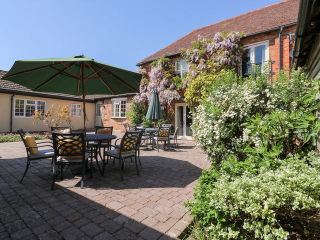 A courtyard with tables and green umbrellas surrounded by plants and a brick building at BB House in Roxhill Manor Farm