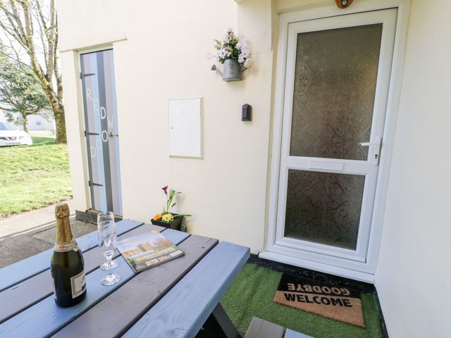 A picnic table with a bottle of champagne two glasses and a magazine outside a door with a welcome mat at Redwood in Harlech