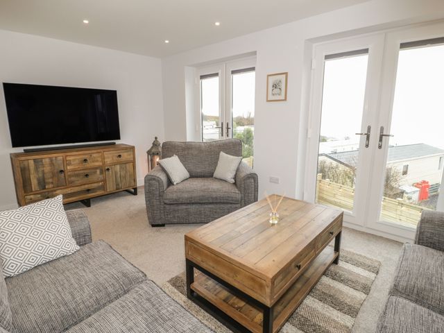 A living room with gray sofas a wooden coffee table tv on a wooden stand and glass doors at The Sandy Bee in Benllech