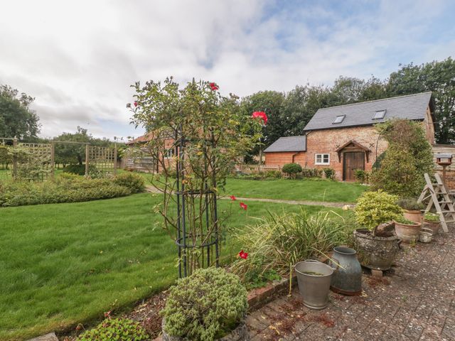 A garden with green grass a brick path potted plants a rose bush and a brick building at The Nest at the Round House in Chitterne near Warminster