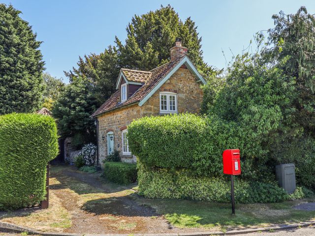 A stone cottage with a tiled roof surrounded by hedges and trees with a red postbox in front at Old Blacksmiths Cottage in North Willingham Near Market Rasen