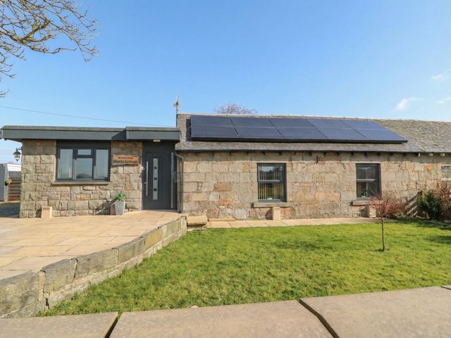 A stone building with solar panels and green lawn at Shotts Cottage Stirling