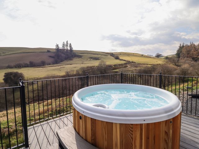 A hot tub on a deck overlooking fields and hills at The Sheep Shed in Llanrhaeadr-Ym-Mochnant