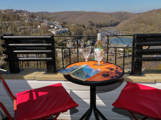 A balcony with a round table and two red chairs overlooking a river and houses at The Knoll in Looe