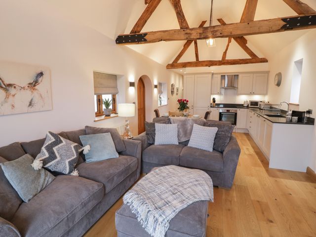 An open plan living room and kitchen with wooden beams on the ceiling sofas and a dining table at The Parlour in Droitwich Spa