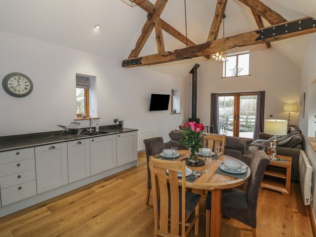 An open-plan kitchen and living area with a dining table set with plates and glasses and a vase of flowers on top a sofa a wood-burning stove and exposed wooden ceiling beams at The Parlour in Droitwich Spa