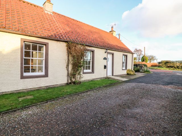 The exterior of a single-story house with a tiled roof grass along the front and a gravel driveway at Rhum Cottage Peat Inn near St Andrews