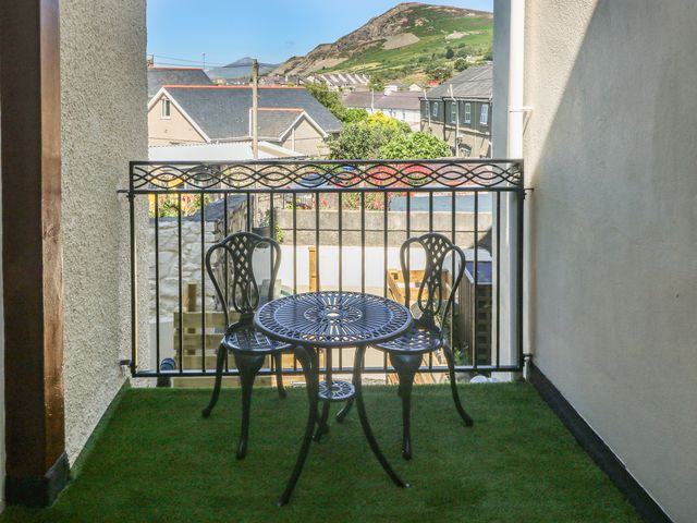 A small balcony with a black metal table and two chairs and a view of houses and hills at Gwenallt in Nefyn