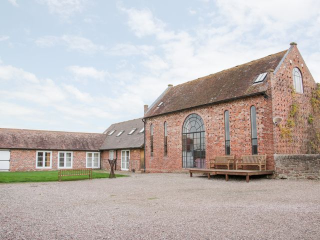 A brick building with large arched windows benches on a wooden deck and a gravel courtyard at Windy Mundy Farm in Pitchford near Shrewsbury