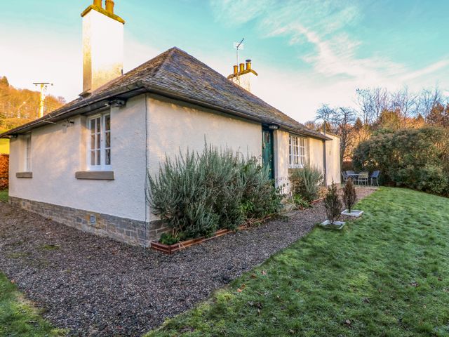 A single-story house with white walls and a stone roof surrounded by grass and shrubs at East Cottage - Tarvit in Cupar Fife