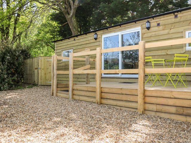 A wooden deck with a small table and chairs outside a wooden cabin at Harvest Lodge in Wineham near Bolney