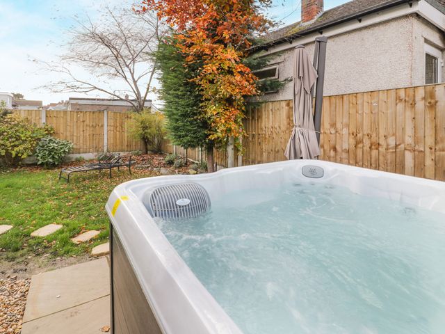 A backyard with a hot tub a folded umbrella a lawn with autumn leaves and a wooden fence at Hilltops in Deganwy
