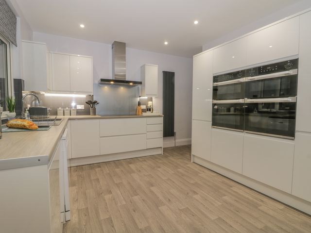 A modern kitchen with white cabinets wooden floors built in ovens and a bread loaf on the counter at North Beach Lodge in Scarborough