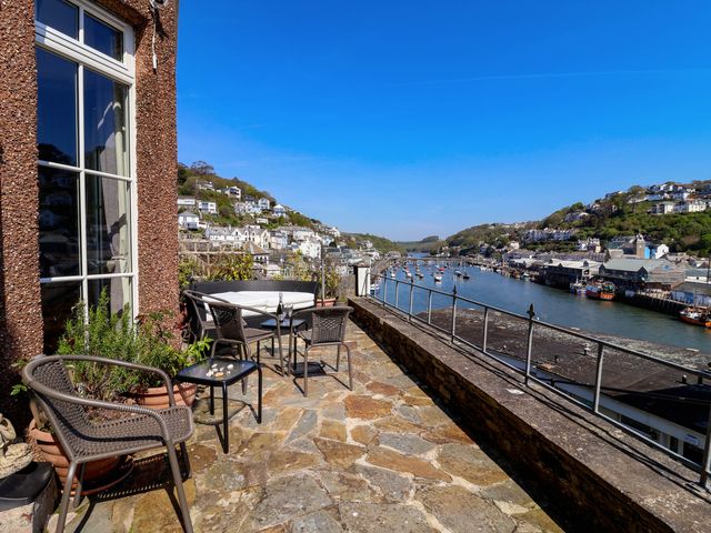 A terrace with wicker chairs and a small table overlooking a river with boats and houses on hills at Albany in Looe